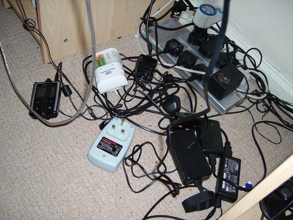 A tangle of British plugs, power adaptors and a multi way extension lead on a carpet